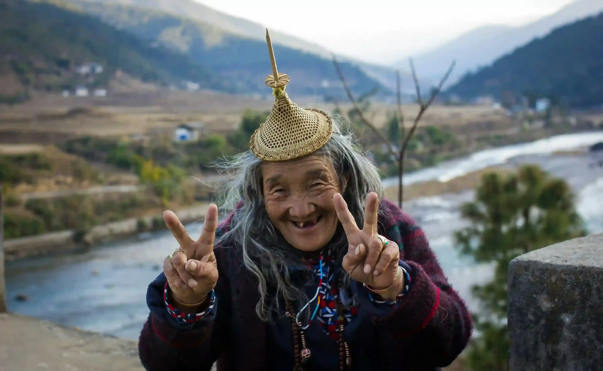 Femme souriante portant un chapeau tressé devant une vallée du Bhoutan